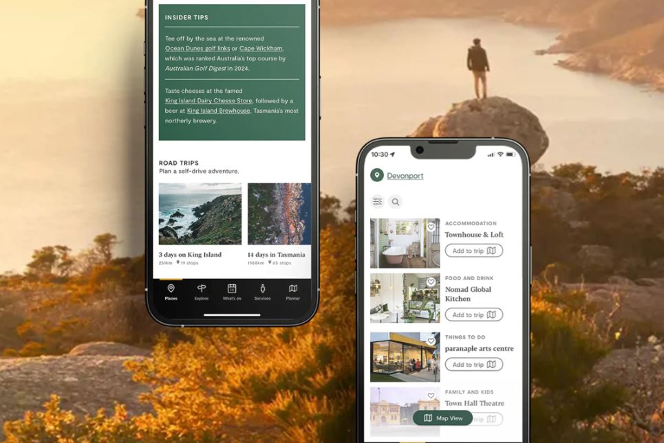 Two phone screens show the Discover Tasmania app display. The upper-left screen shows a series of insider tips and road trips, with photos of Tasmanian destinations and itinerary headlines. The lower-right phone displays Devonport accommodation and food and drink listings, next to photos of these businesses and a button asking to "Add to trip". Behind these two phones as the background image is a man standing on a rock in the golden sunlight, high above the water.