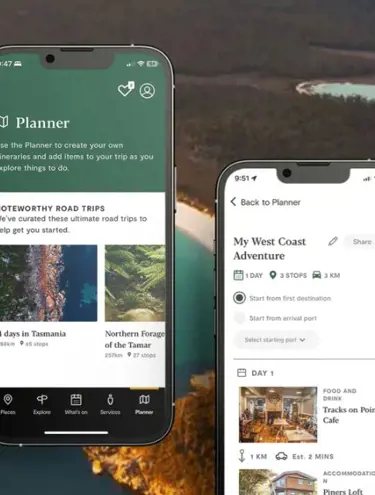 A backdrop image shows the turquoise water and white sand of Wineglass Bay from above, surrounded by lots of gum trees. In the foreground is two phone screens. The screen on the left shows the Discover Tasmania App "Planner" display screen, showing "Noteworthy road trips" and thumbnail images of various Tasmanian locations followed by Itinerary names, such as "14 days in Tasmania". The right-side phone screen displays a personalised trip plan in the app, with the headline "My west coast adventure" followed by information such as "1 day, 3 stops, 3km" and images of each stop on the road trip. The first stop on the road trip reads: "Day 1: Food and drink, Tracks on Point Cafe" accompanied with a photo of the cafe.