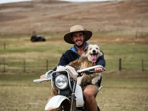 A farmer smiling with his working dog on a farm motorbike, Curringa Farm at Hamilton in Tasmania's Central Highlands