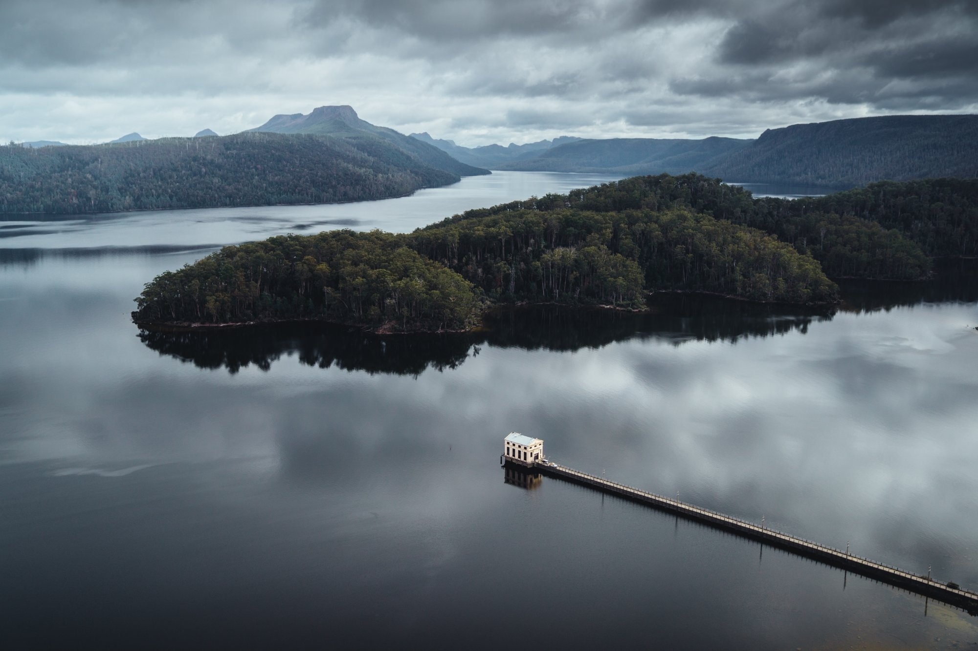 Pumphouse Point jetty extending across mirror still Lake St Clair under moody skies, Tasmania