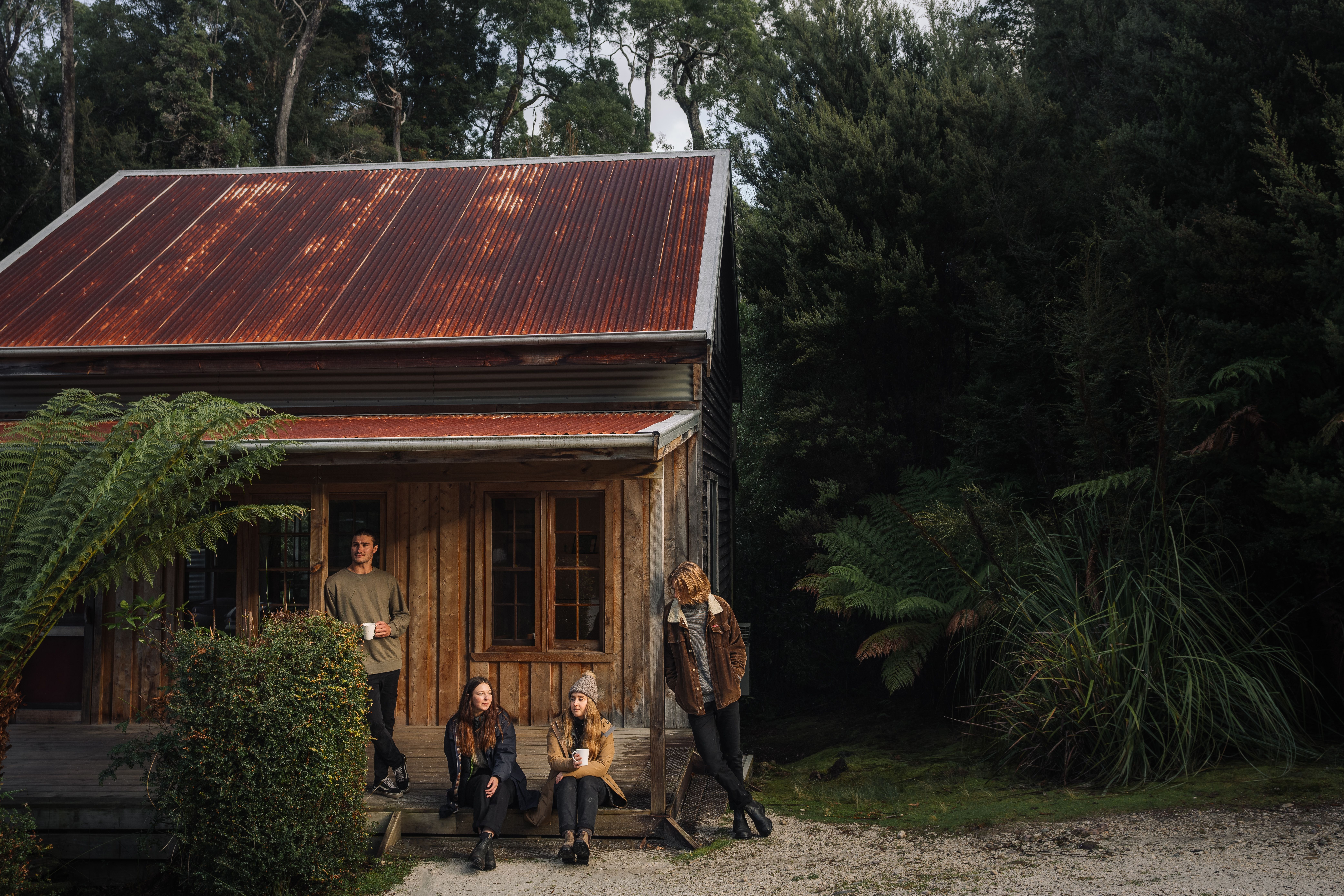 Guests on the porch of a timber miners cottage at Corinna Wilderness Village, takayna / Tarkine, Tasmania's West Coast