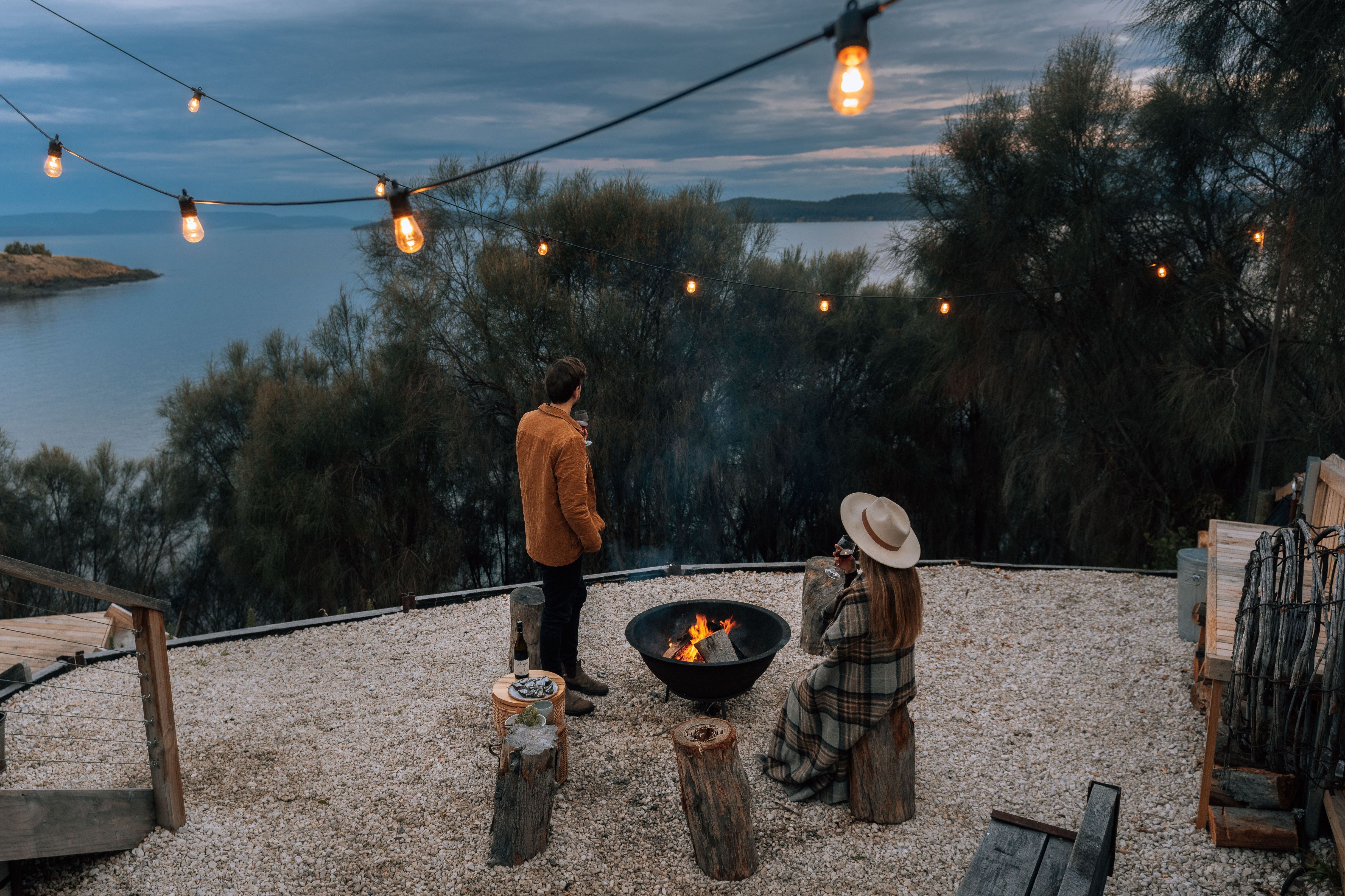 Guests by a firepit and string lights with ocean views at Driftwood Cabin, Primrose Sands, Tasmania
