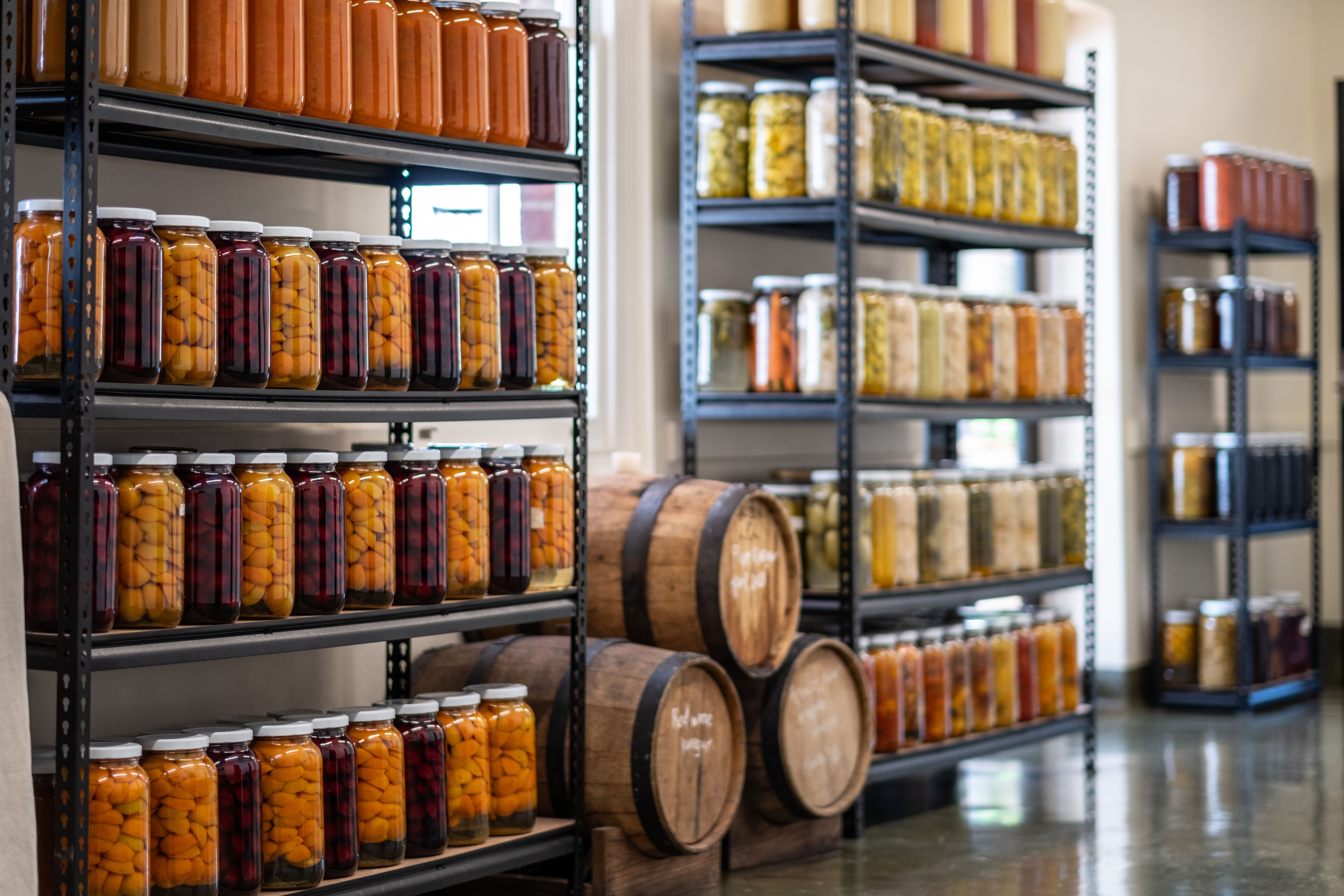 Shelves of preserved produce in glass jars and wooden barrels at The Agrarian Kitchen, New Norfolk, Tasmania