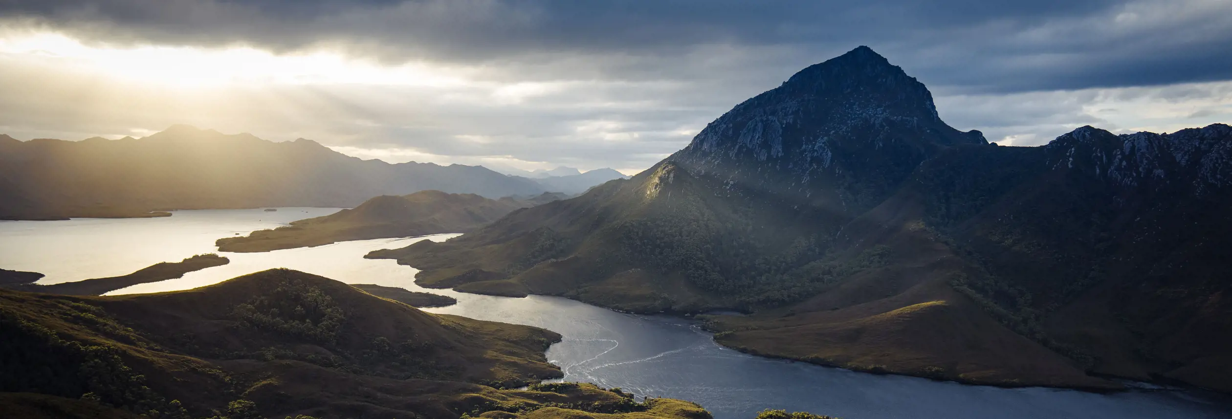 Sunlight breaking through clouds over Bathurst Harbour and surrounding mountains, Southwest National Park Tasmania