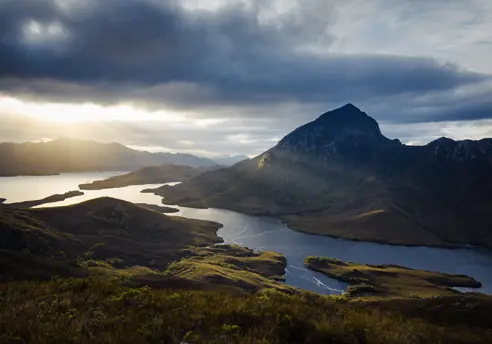 Sunlight breaking through clouds over Bathurst Harbour and surrounding mountains, Southwest National Park Tasmania