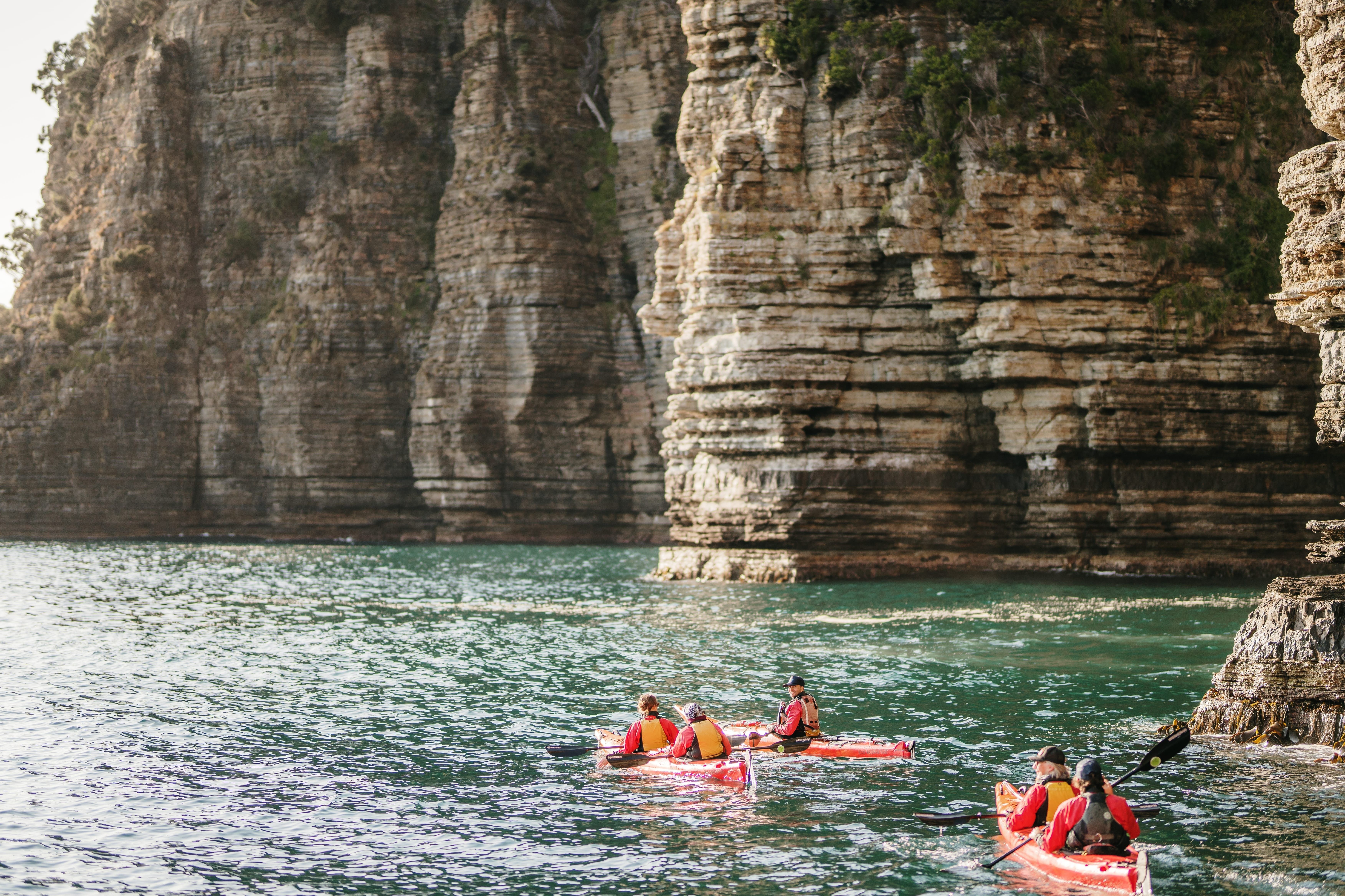 Kayakers paddling beneath tall cliffs with Southern Sea Ventures, Tasman National Park on Turrakana / Tasman Peninsula