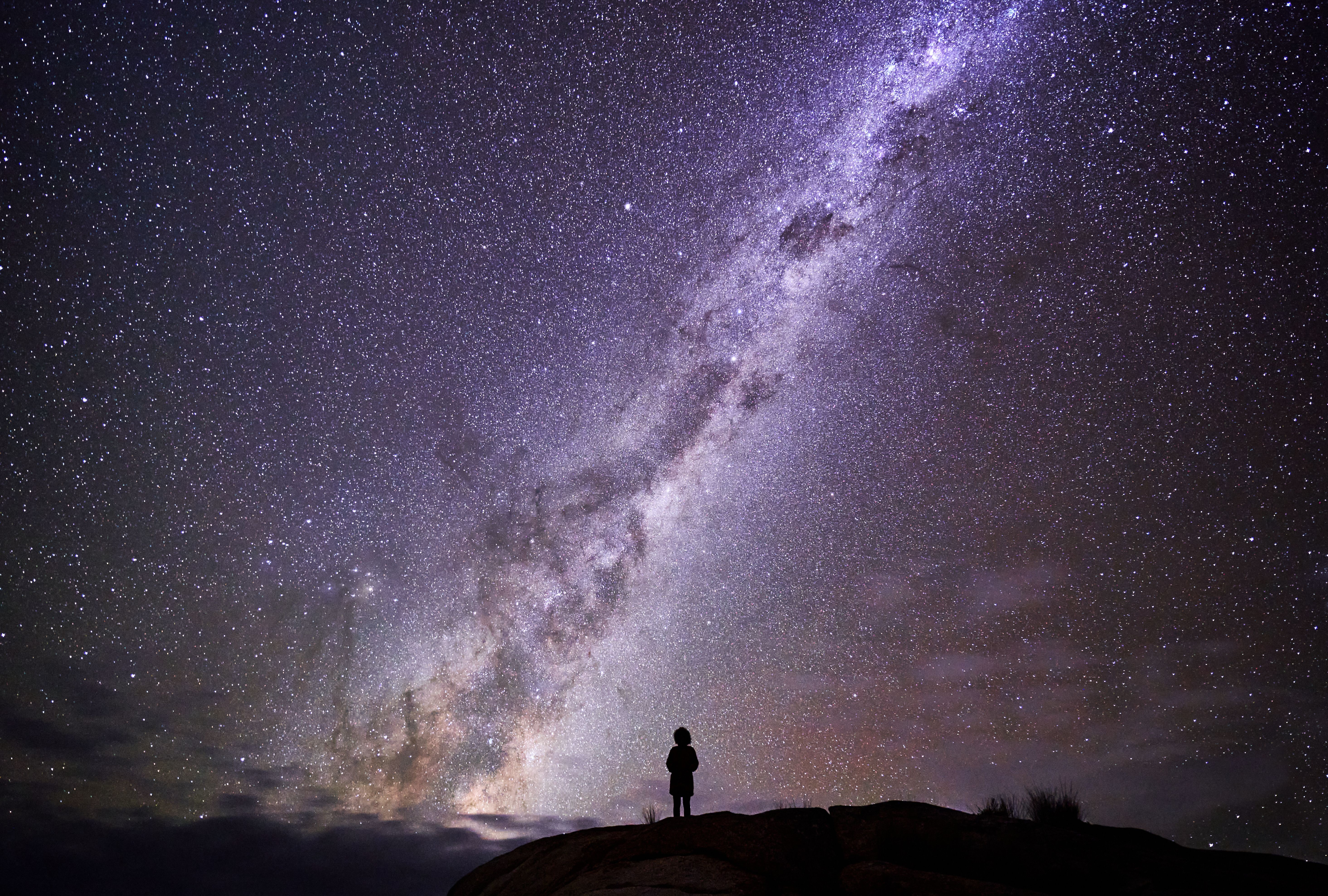 Person silhouetted on a rocky outcrop beneath the Milky Way at larapuna / Bay of Fires area, Tasmania's East Coast