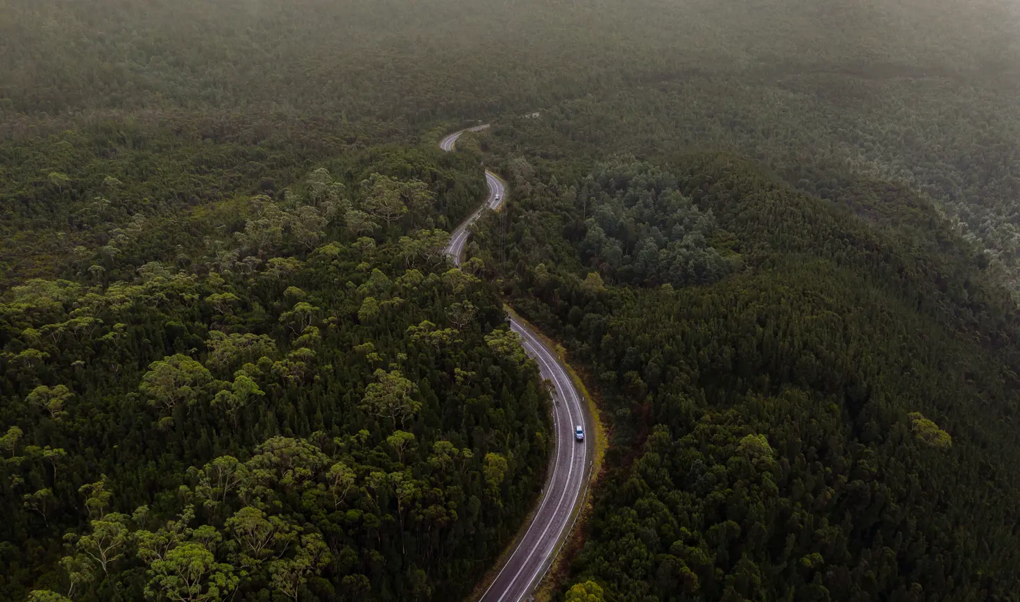 Aerial view of cars winding along Anthony Road surrounded by trees, West Coast Range, Tasmania