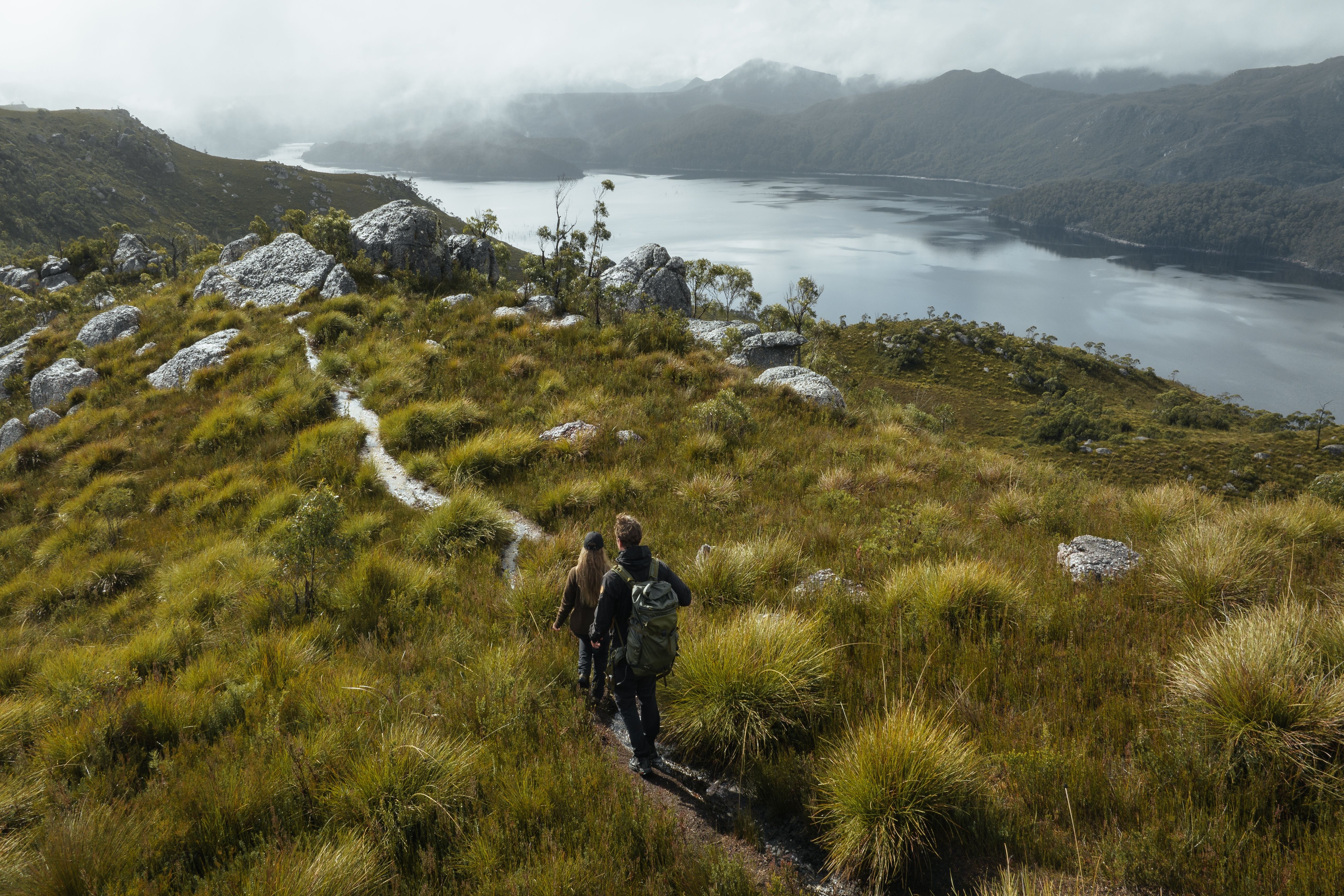 Walkers on coastal scrub land with button grass plains and mountain range in background