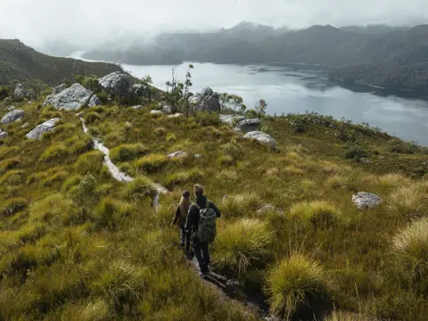 Walkers on coastal scrub land with button grass plains and mountain range in background