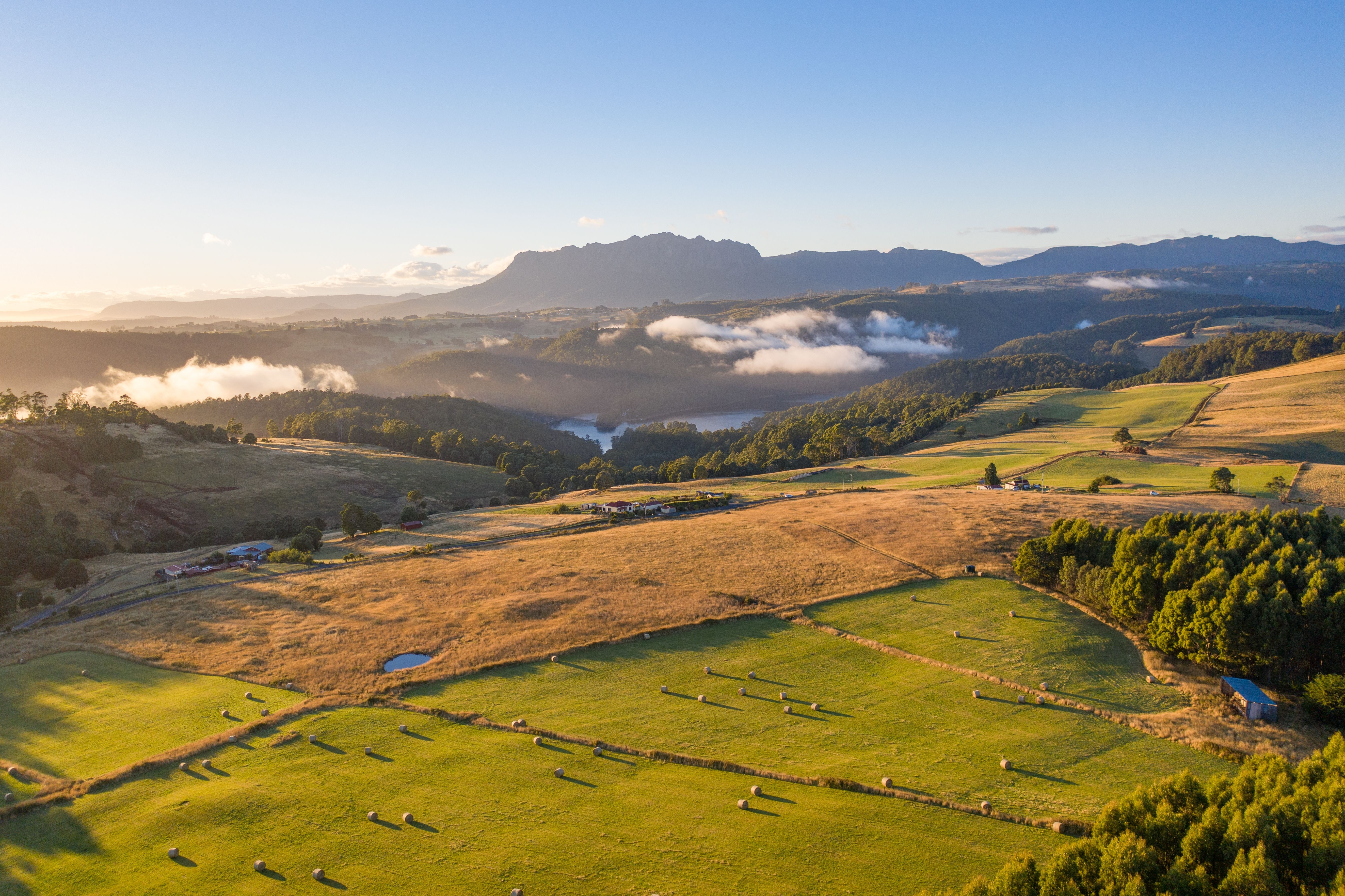 A sweeping view from an elevated vantage point across green farmland, rolling hills and distant coastline, with a prominent mountain rising from the plains.