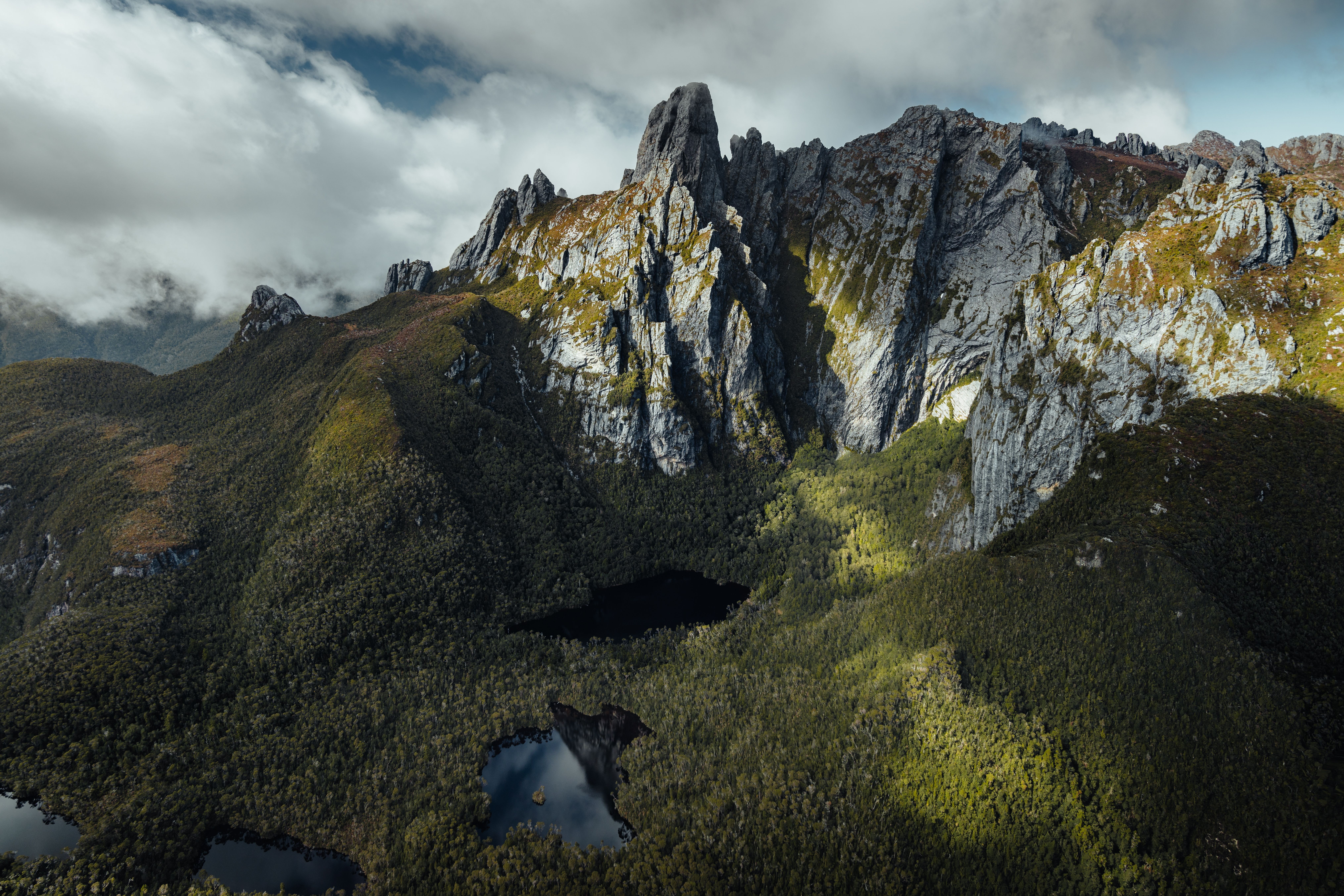 Rugged mountain peaks reaching into dramatic clouds, with golden light catching the rocky slopes and creating deep shadows in the valleys below.