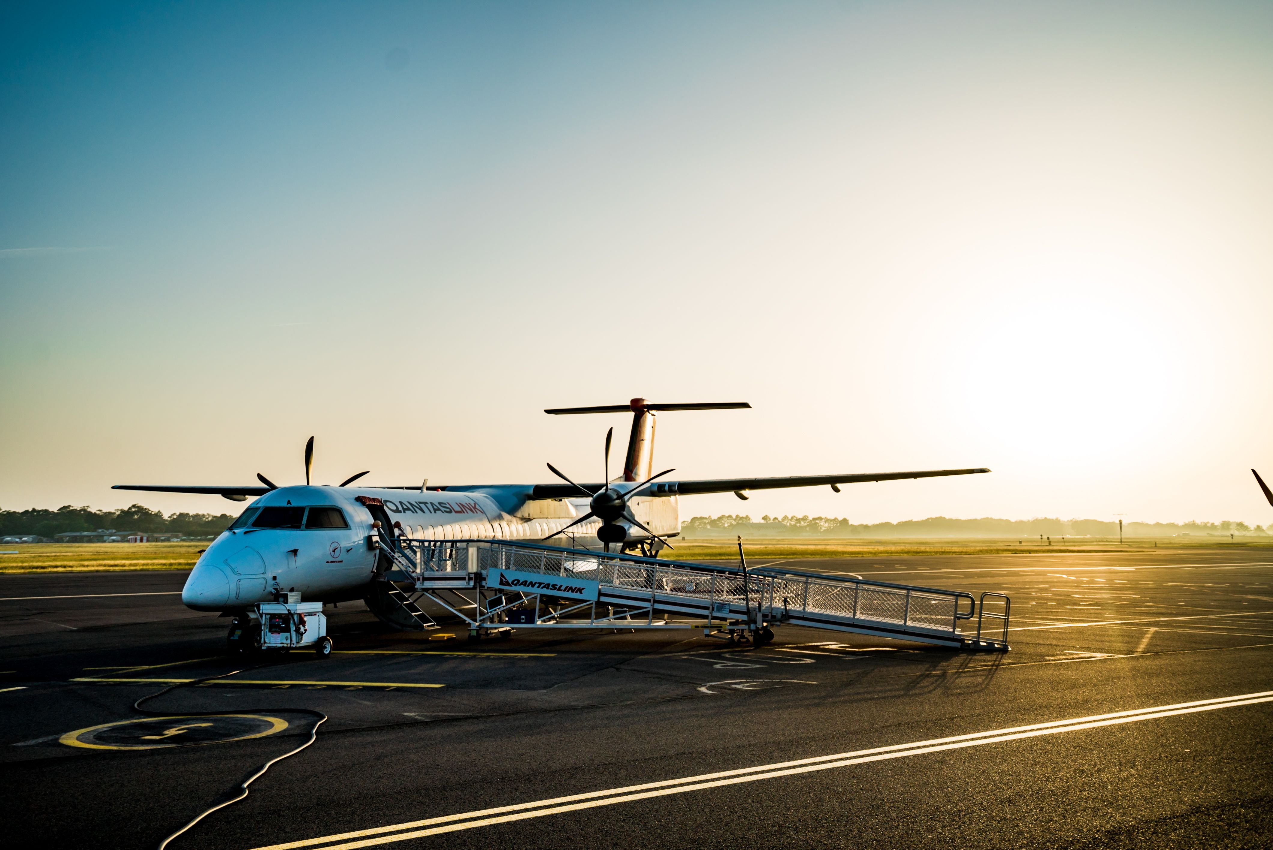A small regional aircraft on the tarmac of an airport, with green rolling hills visible in the background beyond the runway.