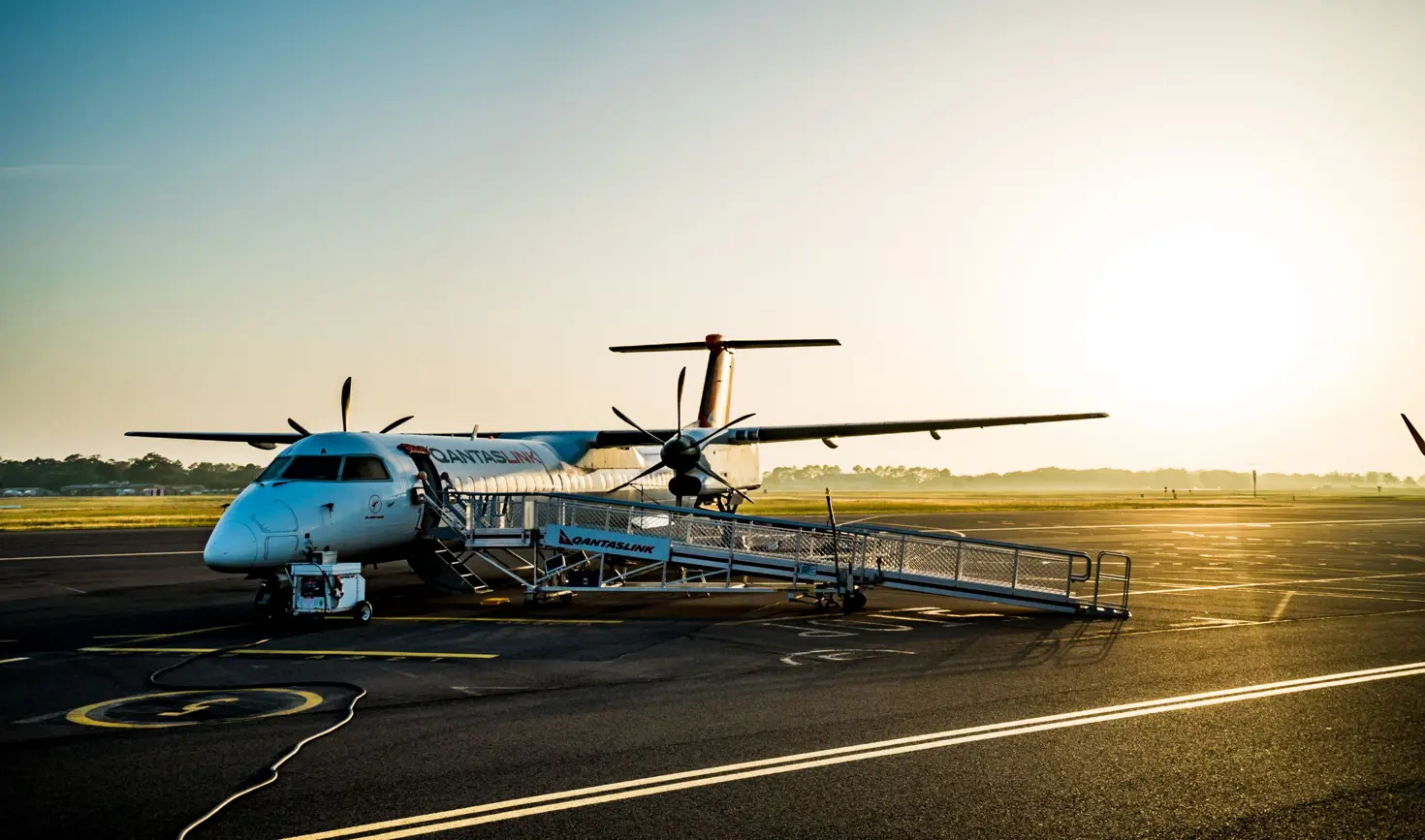 A small regional aircraft on the tarmac of an airport, with green rolling hills visible in the background beyond the runway.