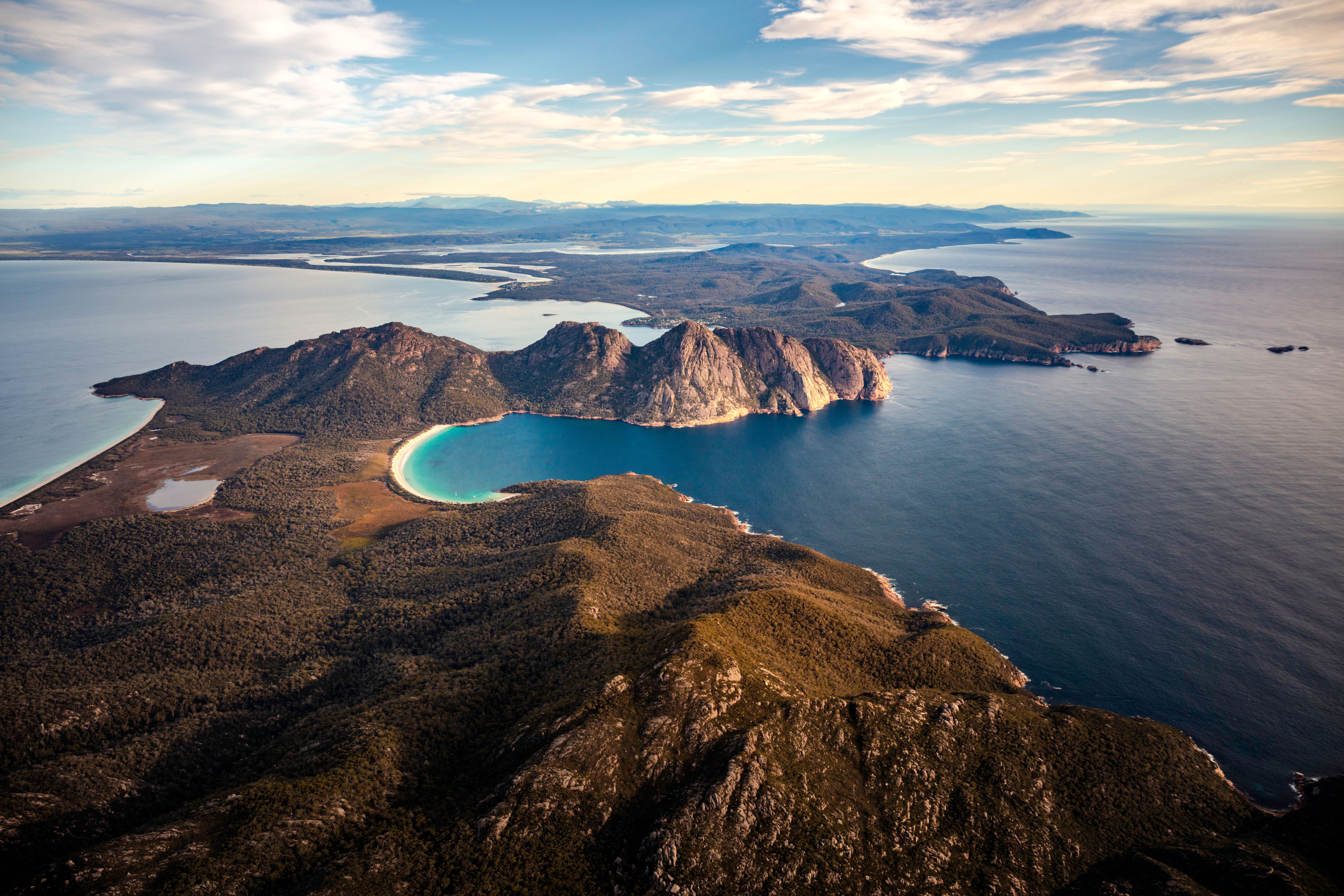 An aerial view of dramatic coastal cliffs dropping away to a crescent of white sand beach and vivid turquoise water below.