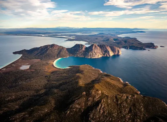 An aerial view of dramatic coastal cliffs dropping away to a crescent of white sand beach and vivid turquoise water below.
